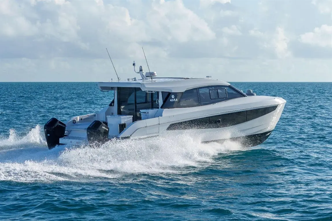 A sleek motorboat speeds through turquoise waters, leaving frothy waves in its wake under a partly cloudy sky.